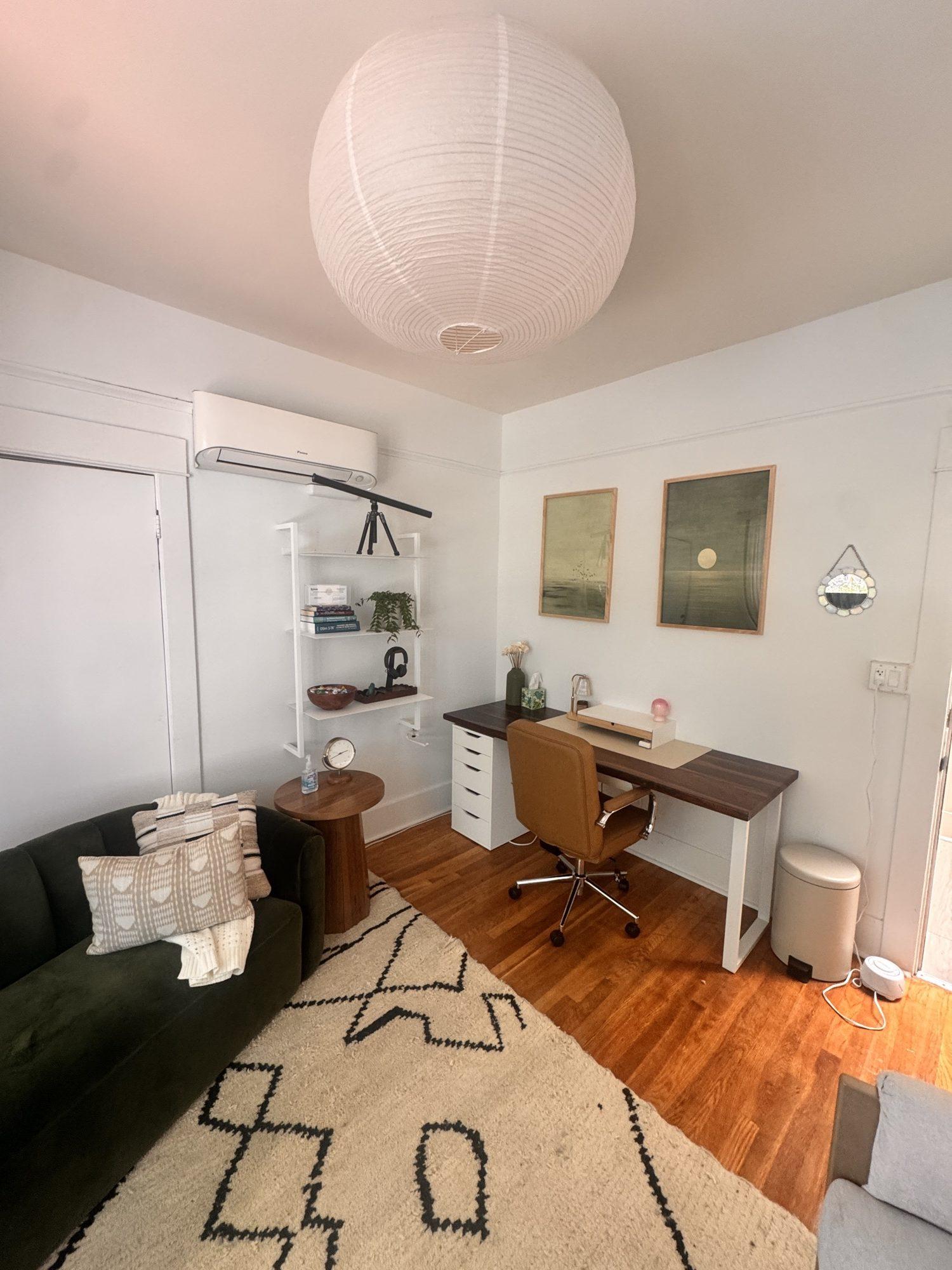 Desk corner with a tan leather chair, framed art, and a wall shelf with books and plants