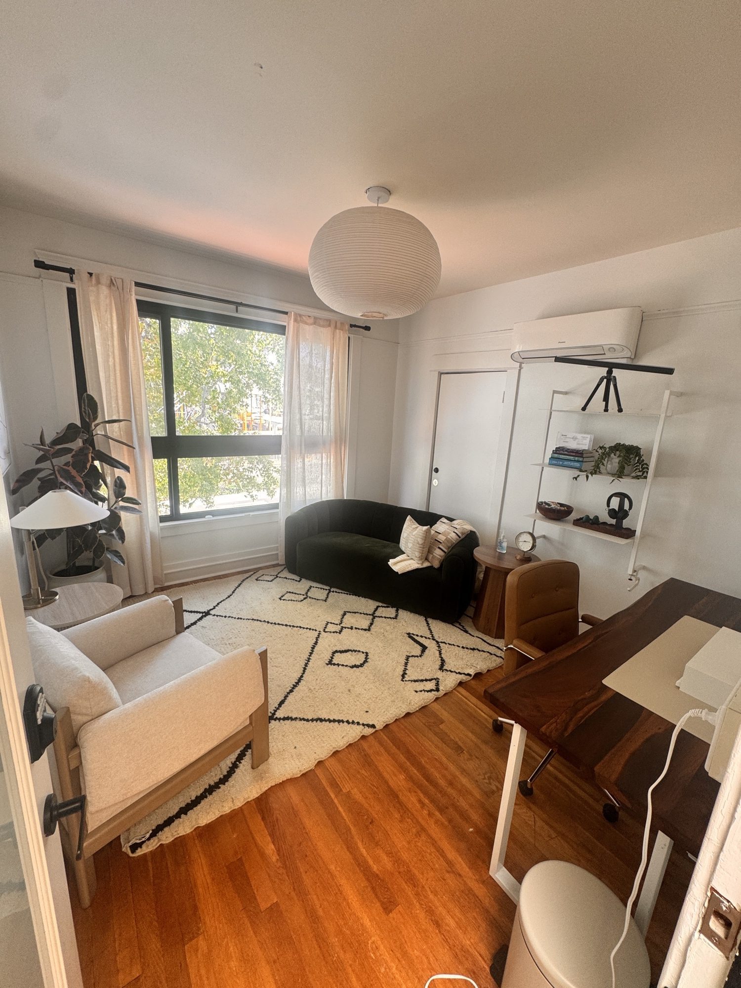 Unit 4 set up for therapy: green velvet loveseat, oak armchair, wool rug and a walnut desk under a big street-facing window